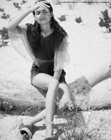 Editorial shot of a woman in a dress sitting on a log with her hand shielding her eyes, in a desert-like setting in black and white.