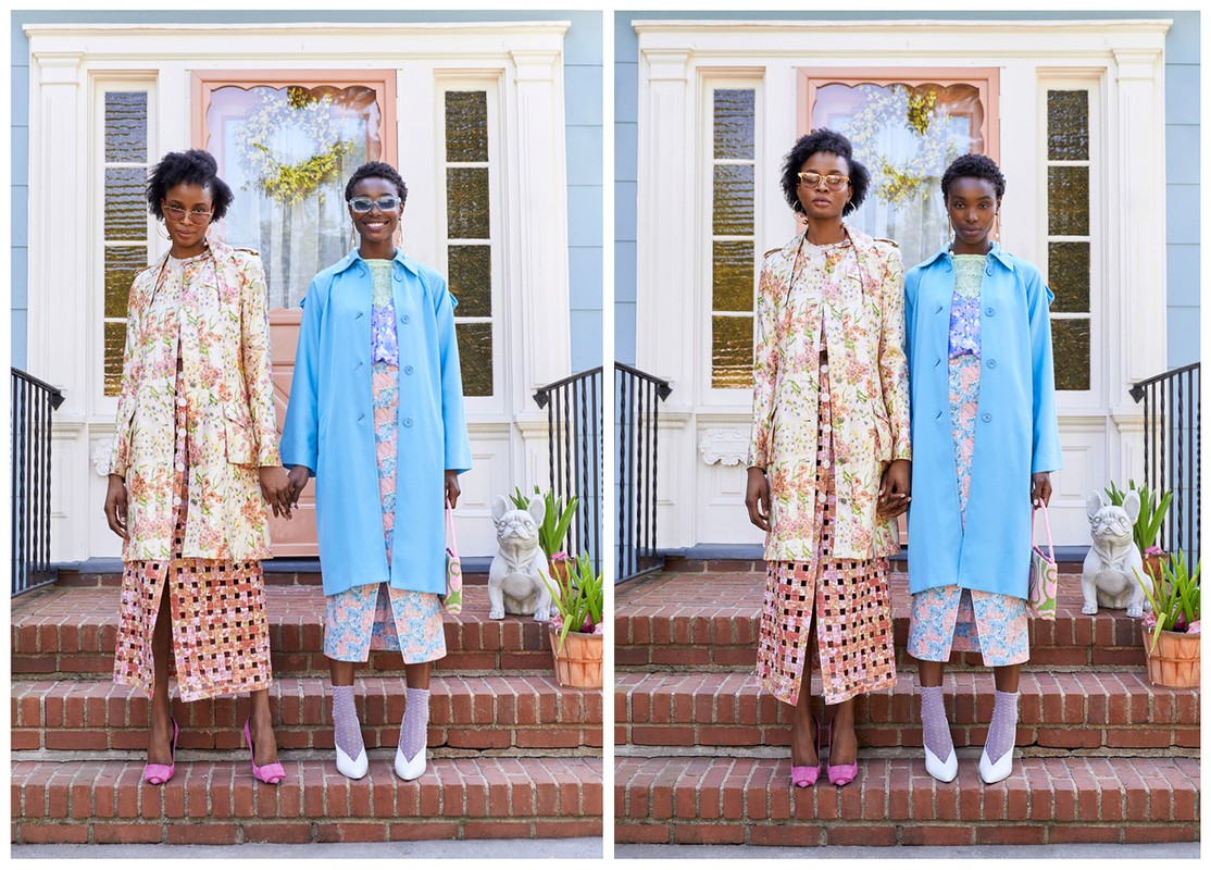 Two African-American women in floral dresses and pastel coats holding hands on brick steps in front of a light blue house with a pink door.