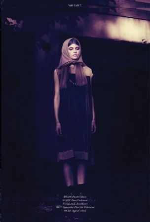 A woman wearing a dark dress and a headscarf standing in a dimly lit setting, styled by Morgan Gibbons.