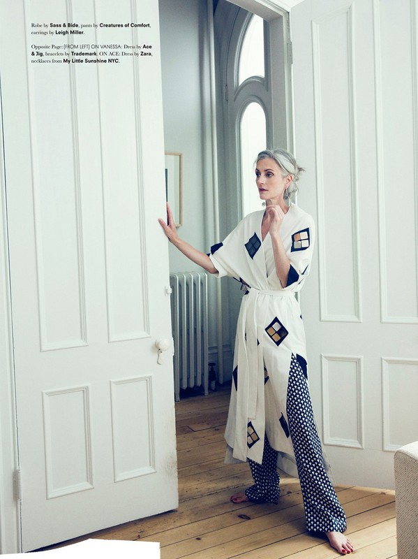 Woman with grey hair in a printed robe standing by white doors in a well-lit home, with hardwood floors and minimal decor.