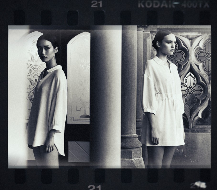 Black and white fashion photograph showcasing two women in white dresses positioned in front of classical architectural elements and designs.