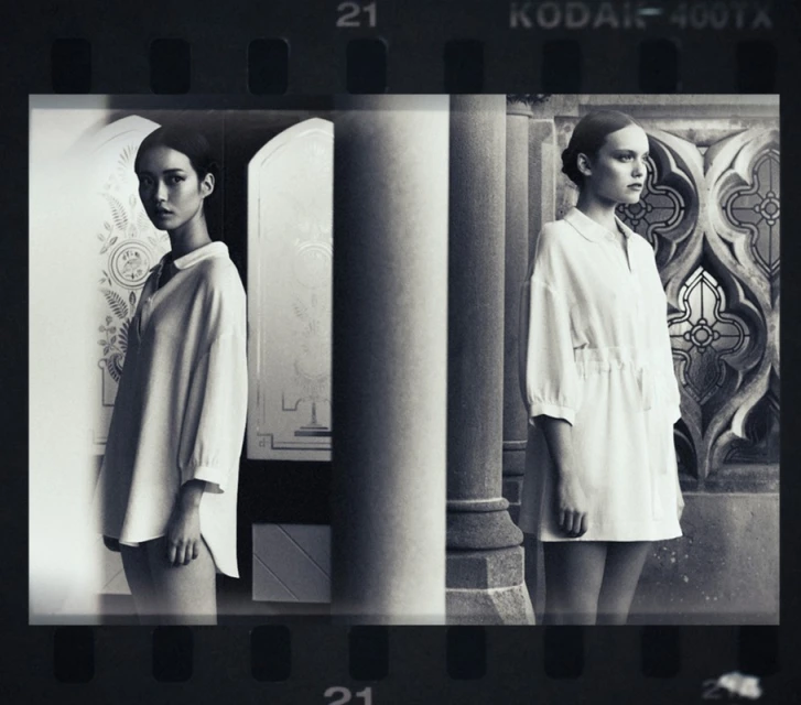 Black and white fashion photograph showcasing two women in white dresses positioned in front of classical architectural elements and designs.
