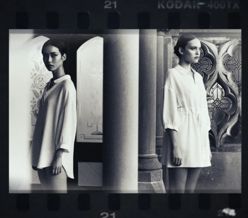 Black and white fashion photograph showcasing two women in white dresses positioned in front of classical architectural elements and designs.