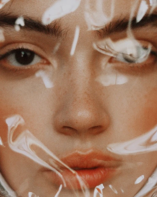 Close-up portrait of a young adult female with light skin, brown eyes, and freckles, partially obscured by transparent plastic wrap.