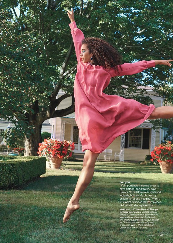 Woman in pink dress jumps mid-air in a grassy yard with a house in the background. Barefoot and arms raised, she exudes joy and freedom.