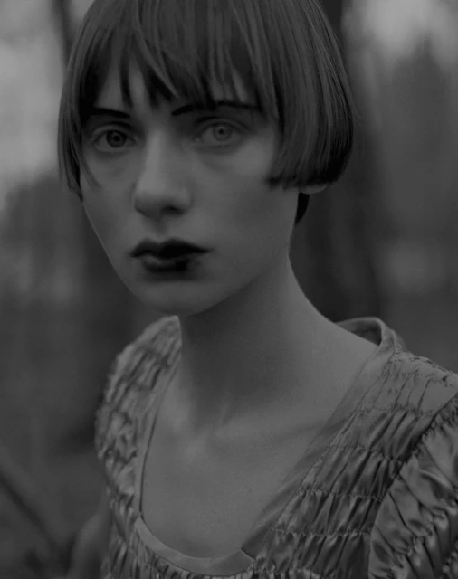 Monochromatic portrait of a young adult female with short bob haircut, wearing a textured dress, captured in an outdoor setting.