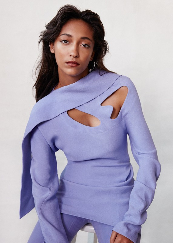 Elegant portrait of a woman in a light purple top with a unique cut-out design, posing in front of a bright white background.