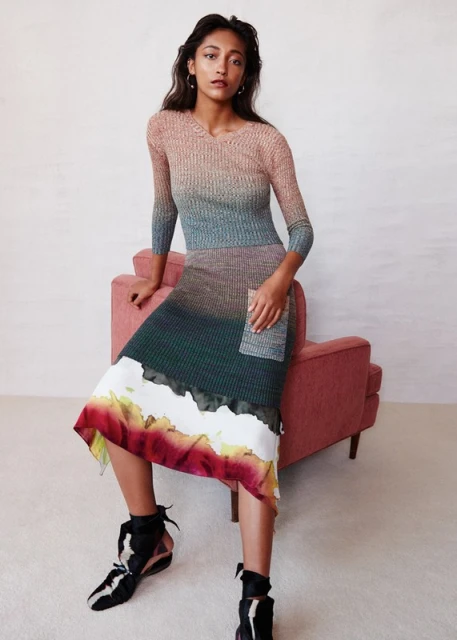 Elegant woman in a multicolored ombre knit dress seated on a pink chair, posing in a studio with ankle-tie heeled shoes for a fashion shot.