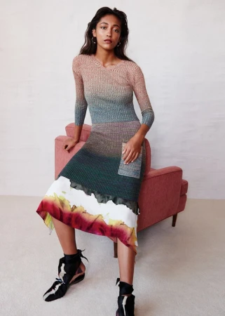 Elegant woman in a multicolored ombre knit dress seated on a pink chair, posing in a studio with ankle-tie heeled shoes for a fashion shot.