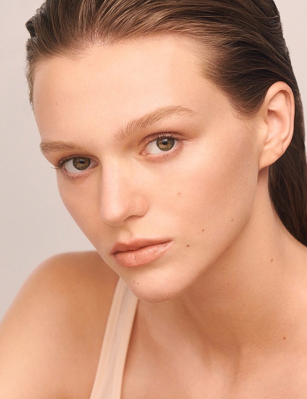 Close-up portrait of a young, fair-skinned woman with sleek, dark hair, natural makeup, and neutral expression against a light background.