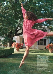 Dancer in a pink dress leaping gracefully across a lush green lawn with a suburban house and trees in the background