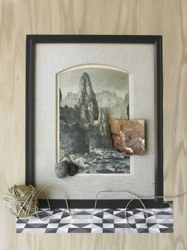 Framed collage featuring a vintage mountain landscape print layered with a rock fragment and wool balls, set against a wood background.