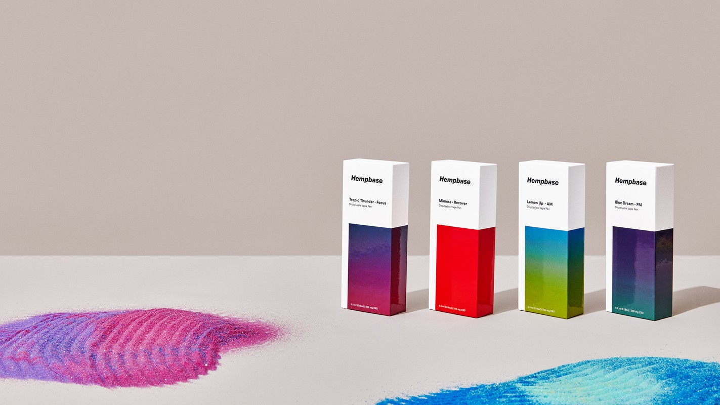 Four Hempbase disposable vape pen product boxes in various colors against a neutral backdrop, with glitter-like material in the foreground.