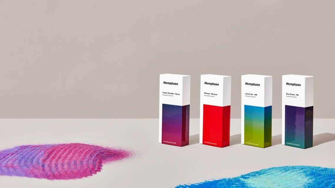 Four Hempbase disposable vape pen product boxes in various colors against a neutral backdrop, with glitter-like material in the foreground.