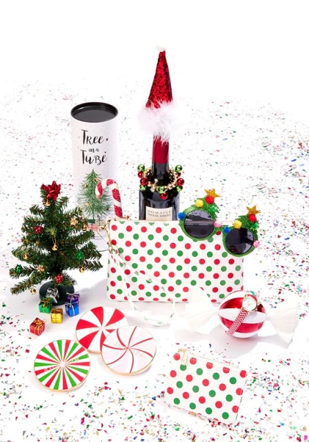Festive flat lay with party favors, clutch, ornaments, and candy on a white surface scattered with confetti for a holiday celebration.