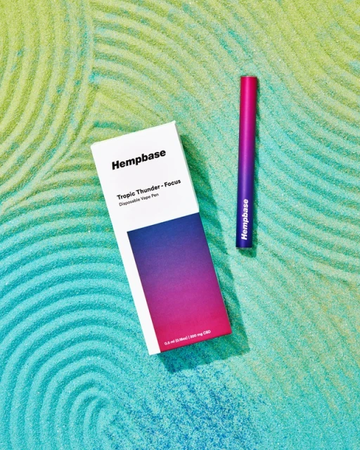 Hemp-based disposable vape pen and product box sit on a textured, patterned surface with gradient blue, green, and yellow colors.