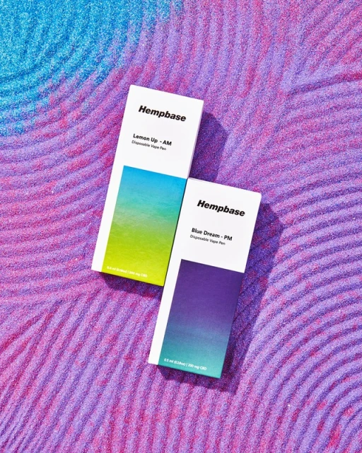 Two Hempbase disposable vape pens on a vibrant purple and blue textured background with concentric circle patterns and gradient colors.