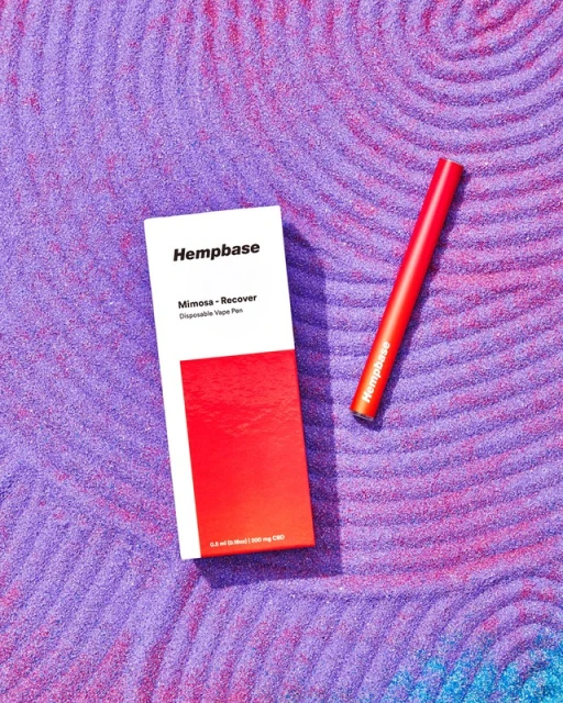 Hemp-based Mimosa Recover disposable vape pen and product box sit on a violet and pink textured surface with concentric circles.