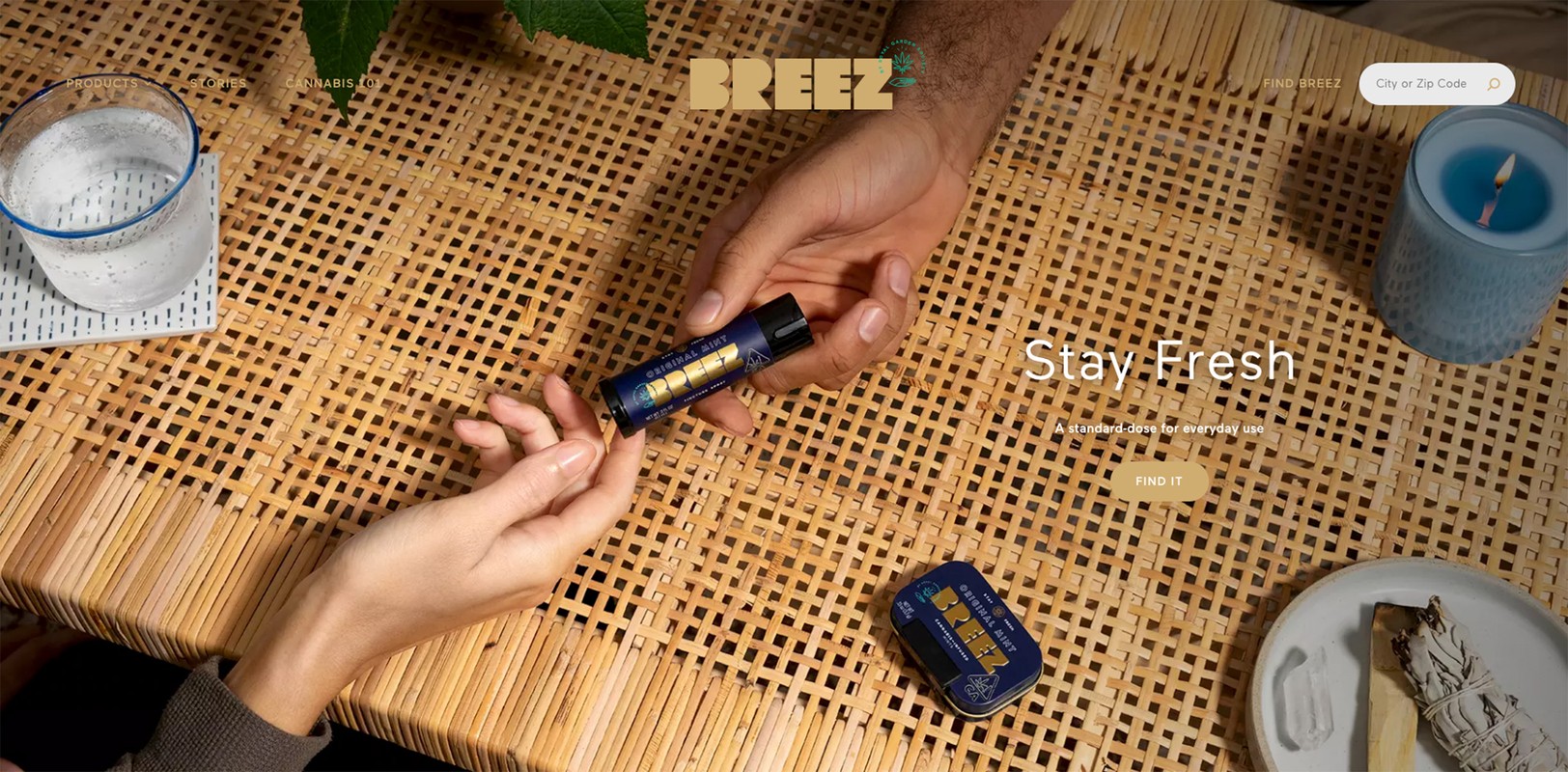 Two hands exchanging a Breez brand THC product on a woven table next to a glass of water and a candle, for the cannabis company's website.