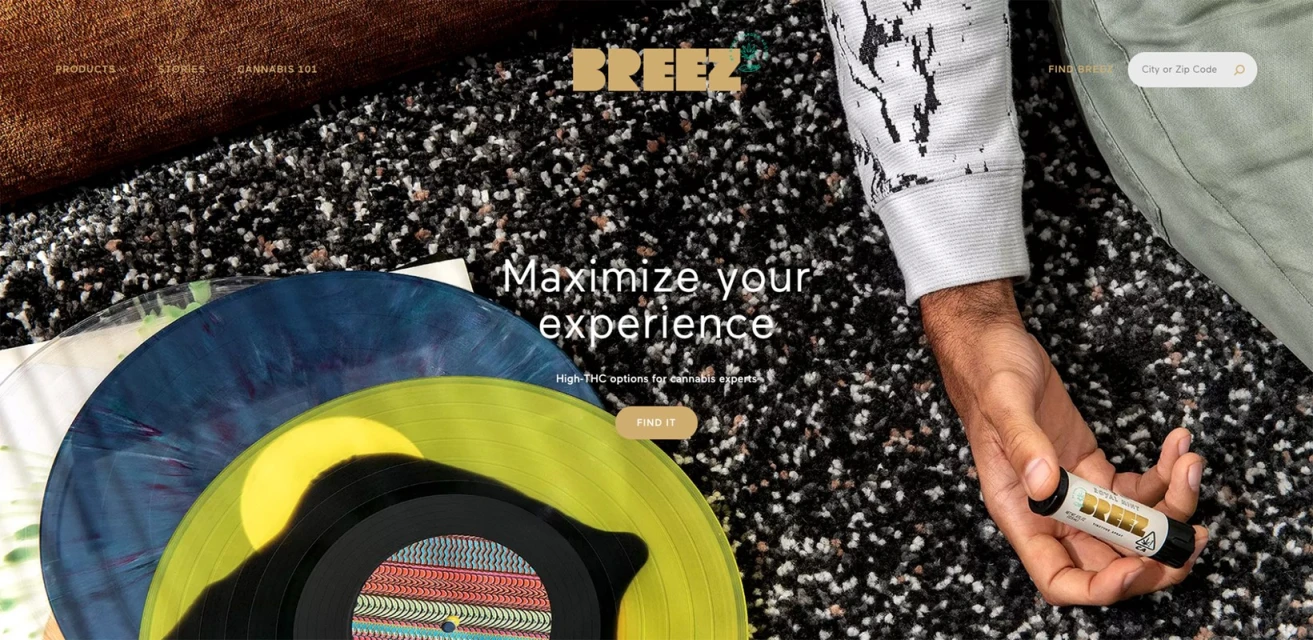 Person holding cannabis product, sitting with vinyl records and carpet in soft lighting. Website text reads: Maximize your experience.