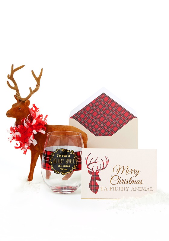 Holiday still life featuring a plush reindeer, wine glass with plaid accent, envelope, and greeting card on a white surface.