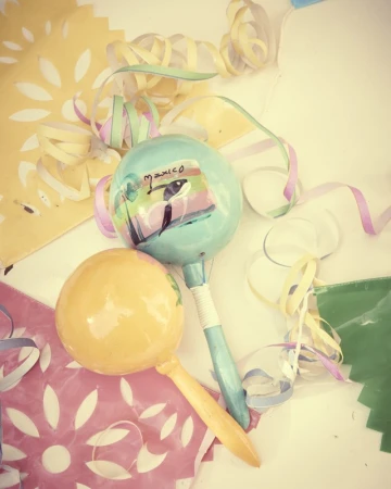 Close-up of two colorful maracas, one light blue with a painting, one yellow, with party streamers and perforated paper.