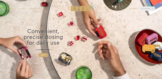 Top-down view of hands interacting with small colourful tins and red dice on a speckled stone table.
