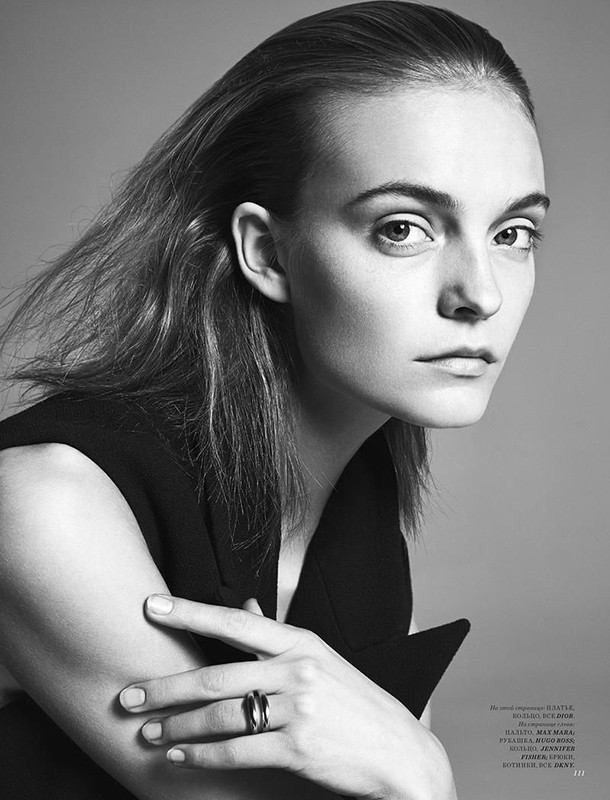 Monochrome portrait of a young woman with dark hair, wearing a sleeveless black top, and a ring on her finger, set against a grey backdrop.