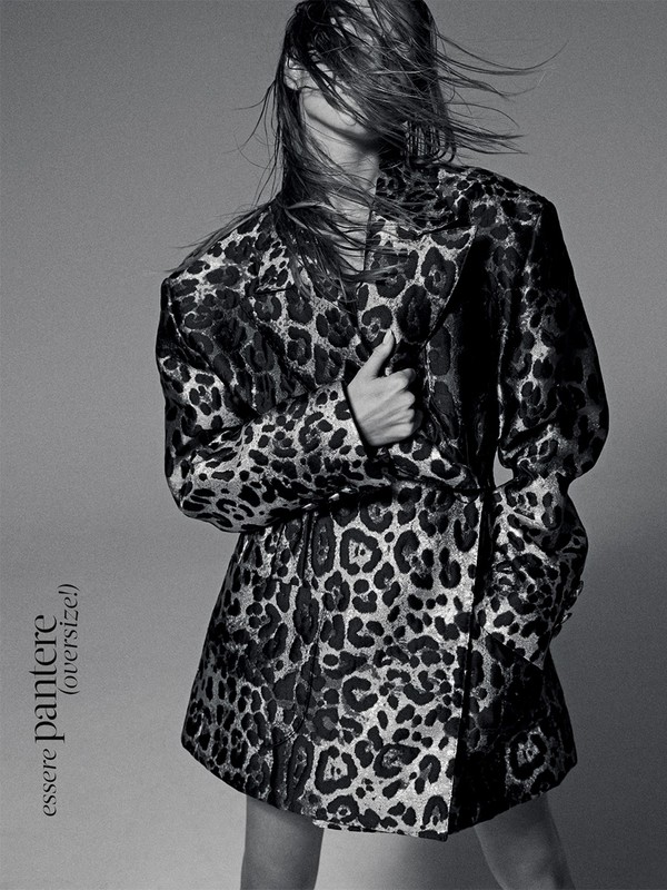 Fashionable woman in leopard-print jacket poses in studio. Wet hair, metallic shine, and grey backdrop create a modern, edgy aesthetic.