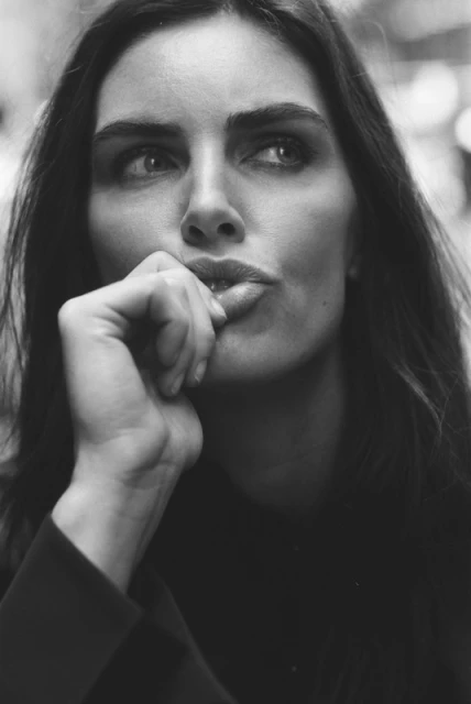Black and white portrait of a woman with dark hair, looking off to the side with her hand near her face in a thoughtful pose.