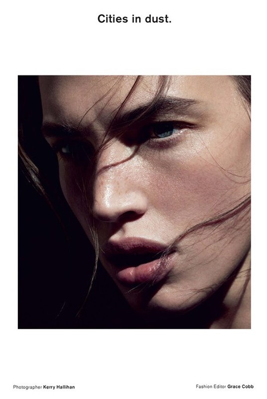 Close-up portrait of a fair-skinned adult female fashion model with loose hair, moody lighting, and dark background in a photo studio.