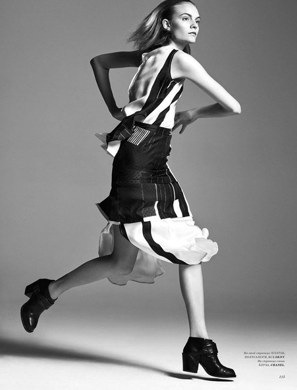 Fashion model in motion wearing a black and white dress with ankle boots, striking a dynamic pose in a studio setting.