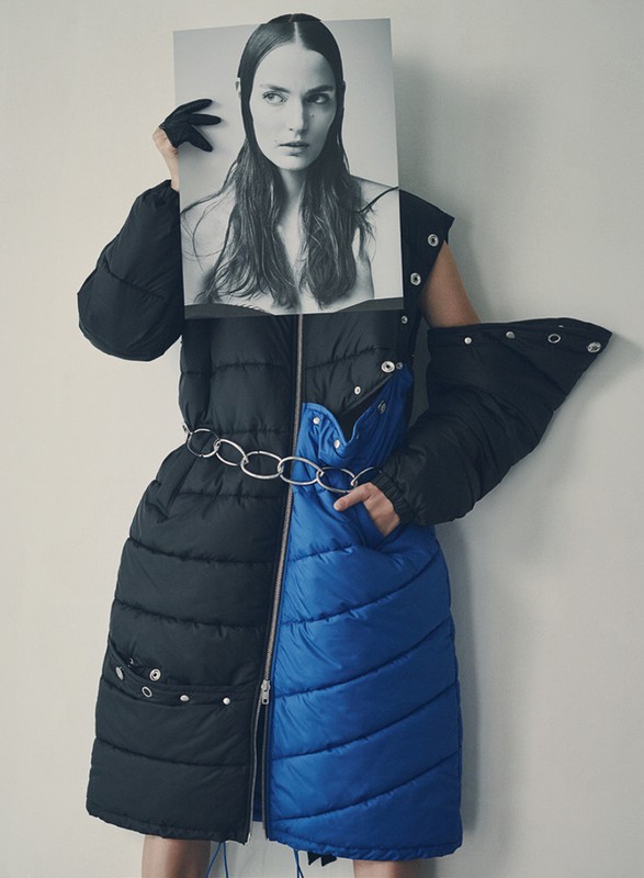 Woman in avant-garde black and blue puffer coat poses with a black and white photo of a model in a studio setting.