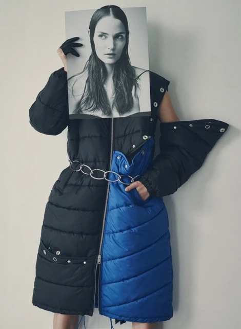 Woman in avant-garde black and blue puffer coat poses with a black and white photo of a model in a studio setting.