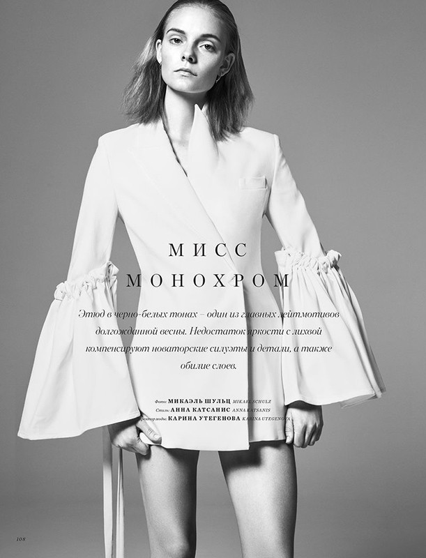 Black and white studio shot of a woman in a stylish white jacket dress with wide sleeves, posing against a plain backdrop.