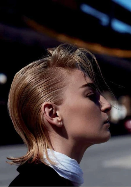 Profile shot of a blond woman in black jacket with a white scarf, outside with soft lighting.