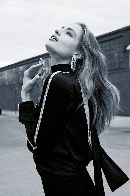 Monochrome portrait of a woman in a black dress with silver accents looking up outdoors against a blurred building and sky backdrop.