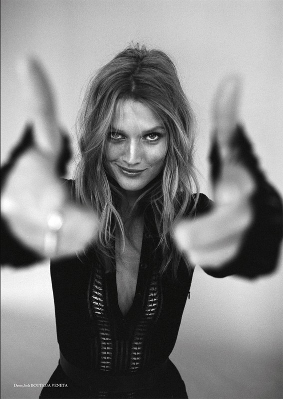 Black and white portrait of a woman with long wavy hair, smiling and holding her hands up to the camera in a photo studio.
