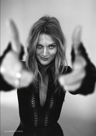 Black and white portrait of a woman with long wavy hair, smiling and holding her hands up to the camera in a photo studio.