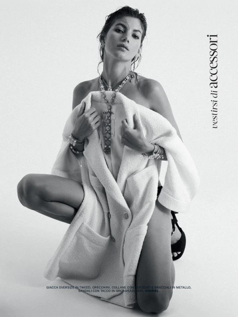 Model crouching against a white background holding a white tweed jacket draped over her shoulders