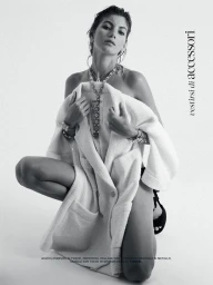 Model crouching against a white background holding a white tweed jacket draped over her shoulders