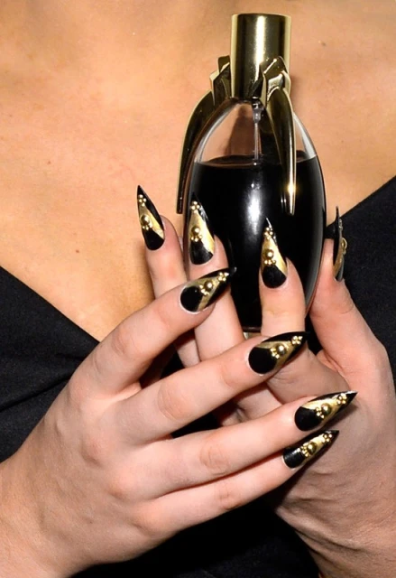 Close-up of hands holding a perfume bottle with black and gold pointy nails. Focus on beauty and cosmetic presentation.