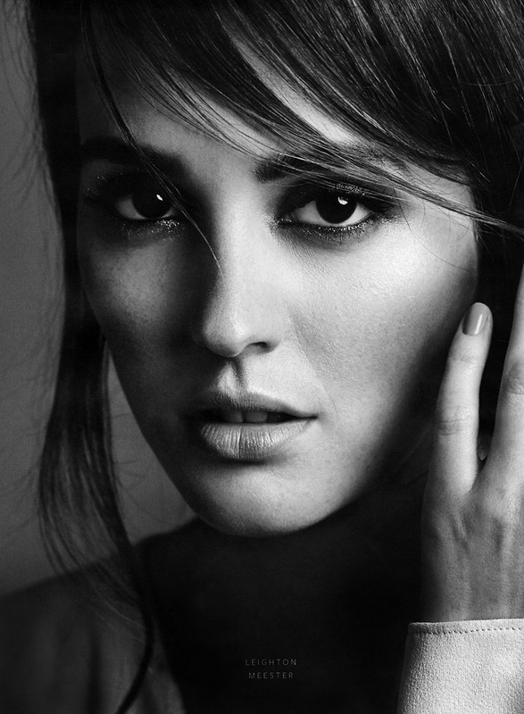 Black and white portrait of a young woman with dark hair, looking directly at the camera with a neutral expression in an indoor setting.