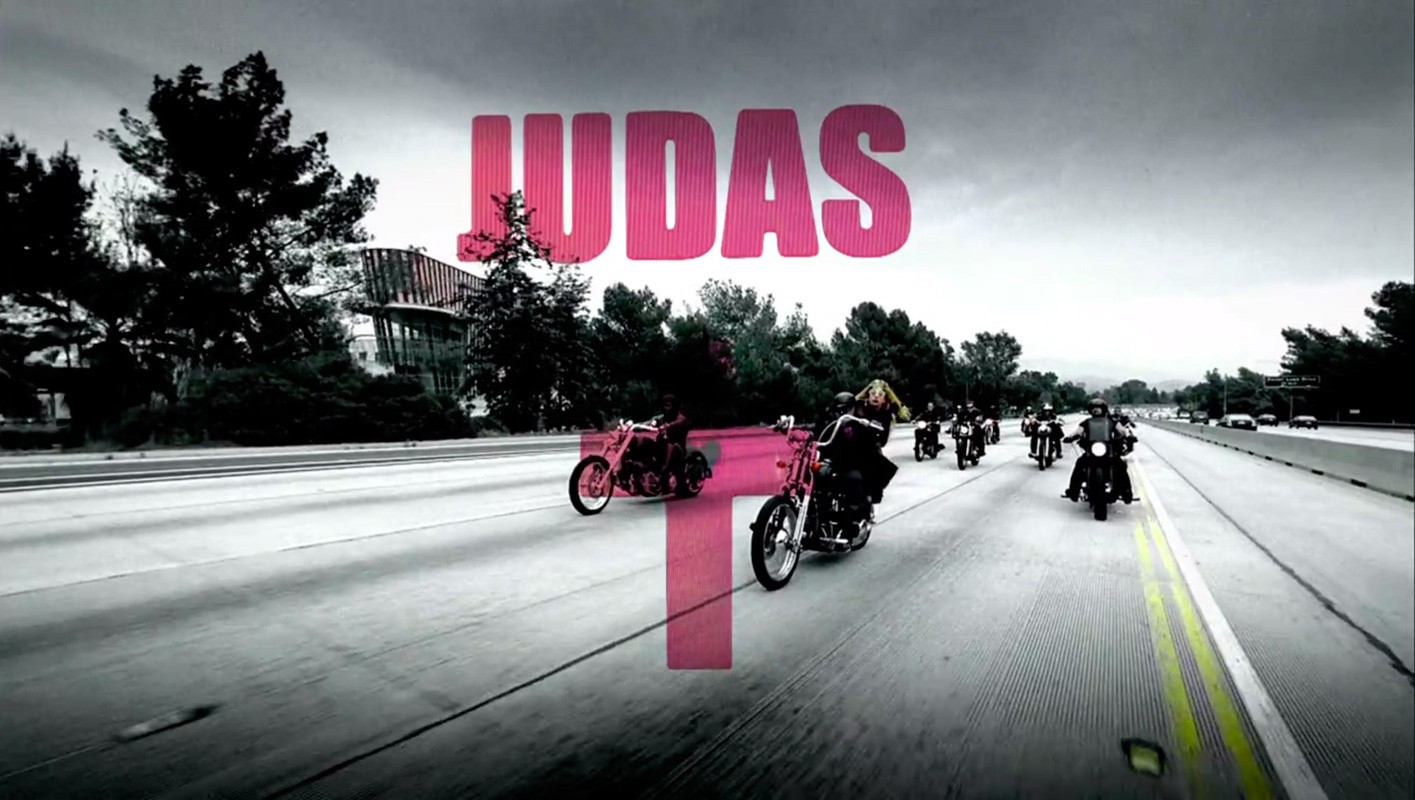 A group of motorcyclists ride in formation on a highway under an overcast sky, with trees and a modern building visible in the background.