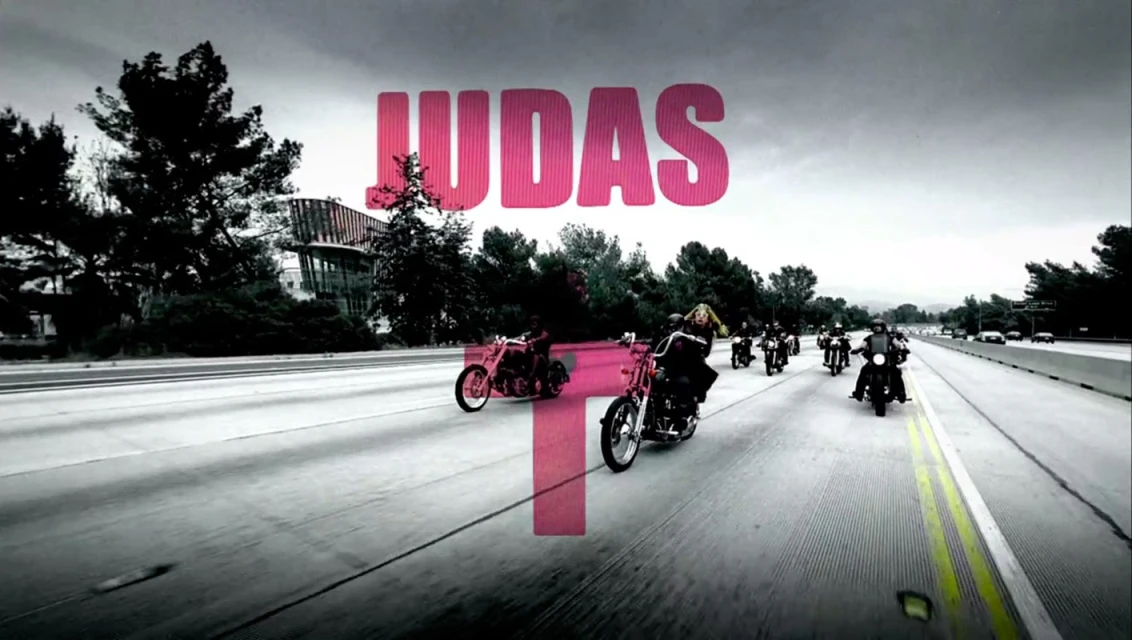A group of motorcyclists ride in formation on a highway under an overcast sky, with trees and a modern building visible in the background.