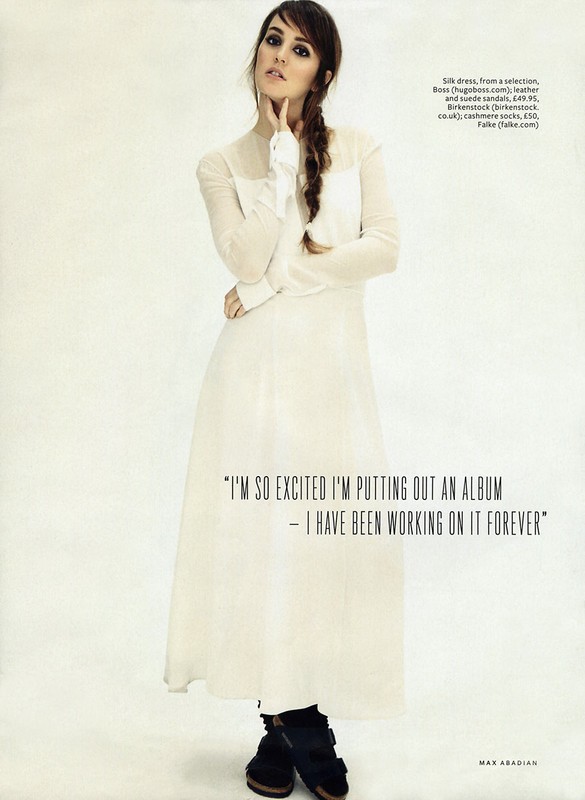 Portrait of a woman in a white dress with a braided hairstyle against a white backdrop, soft lighting, in an indoor studio.