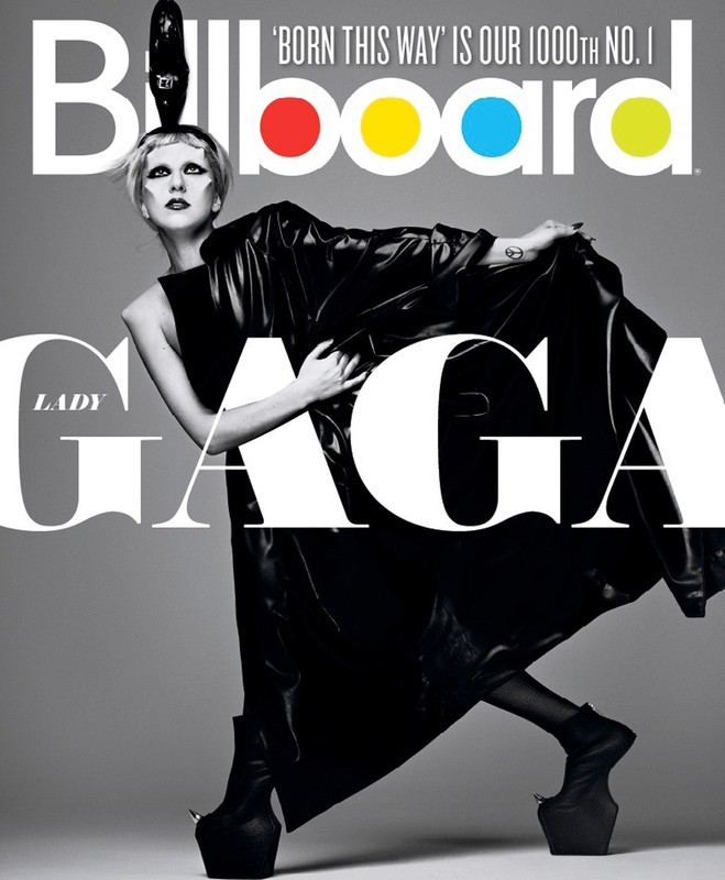 Lady Gaga poses on Billboard cover in black platform boots and a large leather coat, with large text partially covering her figure.