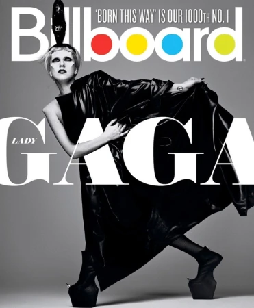 Lady Gaga poses on Billboard cover in black platform boots and a large leather coat, with large text partially covering her figure.