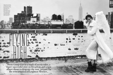 Monochrome fashion editorial featuring a woman with large white angel wings standing on a rooftop overlooking a city skyline.