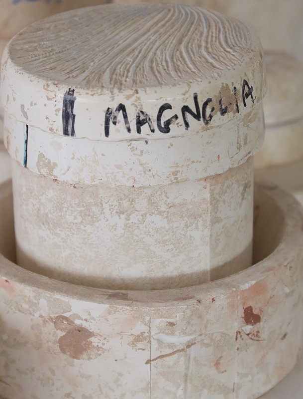 A stacked, weathered white ceramic object with the word 'Magnolia' handwritten on it, shot in a well-lit, indoor setting.